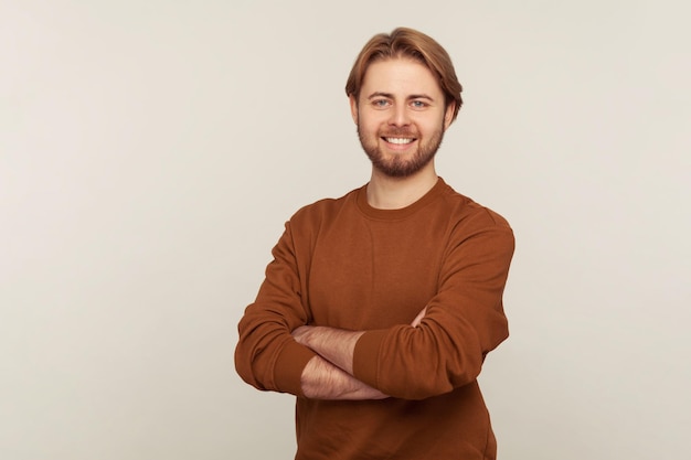 Portrait of happy confident handsome man with neat hair and beard wearing sweatshirt standing, crossing hands