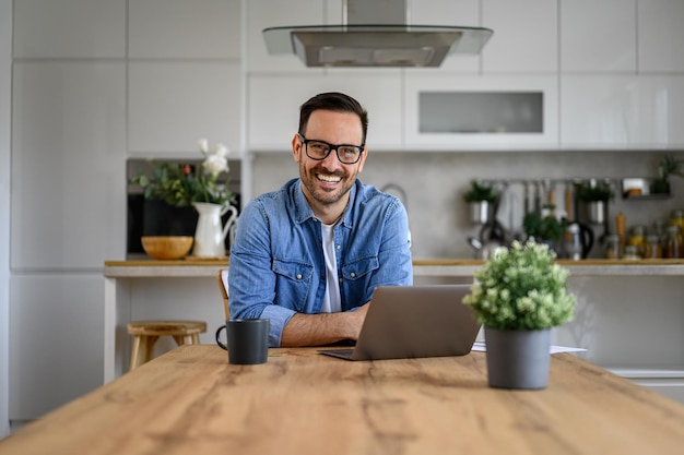 Portrait of happy confident male freelancer with laptop and coffee on desk relaxing at home office