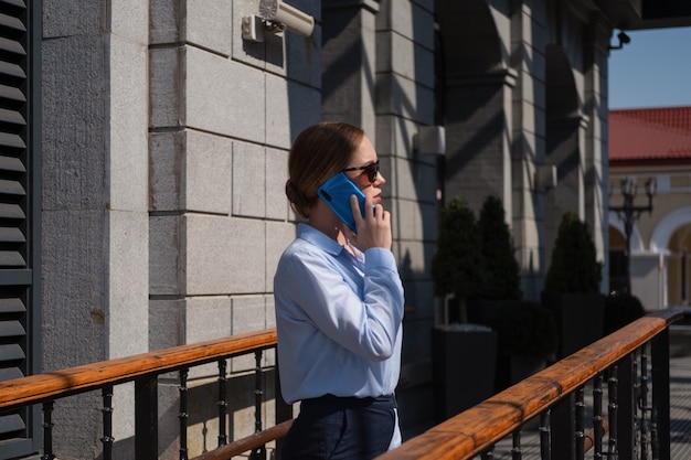 Portrait of happy confident young business woman talking on phone while stand in city outdoor.Millennials life. Light and shadow. High quality photo