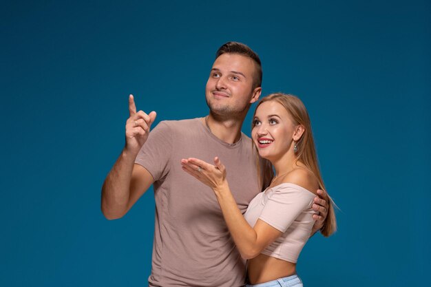 Photo portrait of the happy couple looking and pointing into the distance, isolated on blue background.