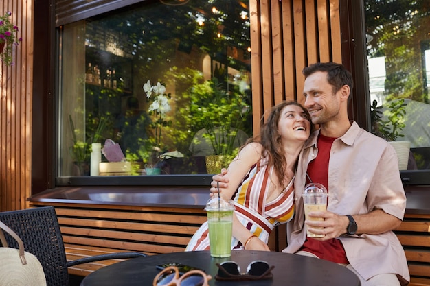 Portrait of happy couple at outdoor cafe looking at each other while enjoying date in summer copy space