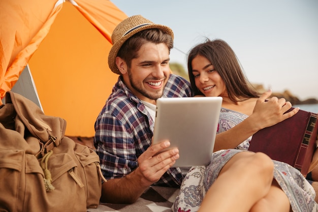 Ritratto di una coppia felice seduta in tenda utilizzando un computer tablet e leggendo un libro