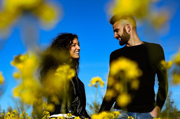 Portrait of a happy couple smiling holding hands looking at each other in a field of flowers in springtime