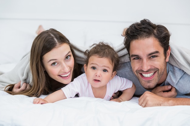 Portrait of happy couple with baby lying on bed 