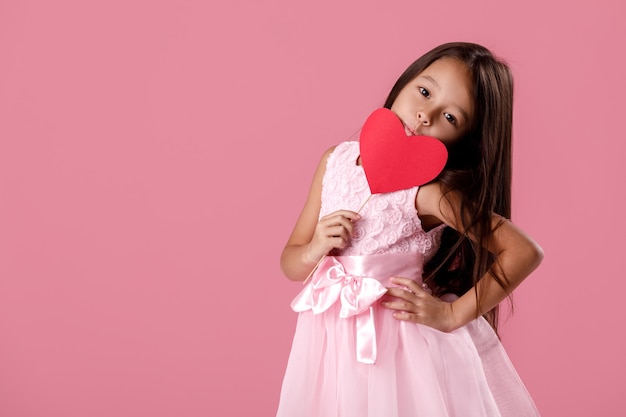 Portrait of happy cute little child girl in a pink dress holding paper heart