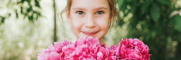 Il ritratto di una bambina felice e carina tiene in mano un mazzo di fiori di peonia rosa