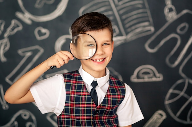 Portrait of a happy cute schoolboy on black chalkboard space