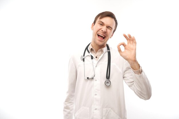 Portrait of happy doctor in white medical coat showing gesture all is well isolated on white background with copy space