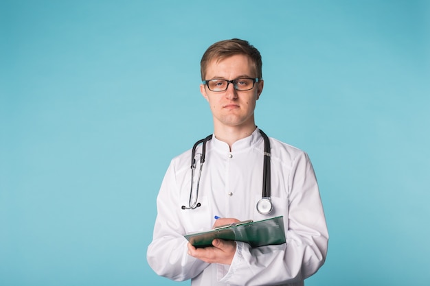 Portrait Of Happy Doctor Writing On Clipboard against a blue background