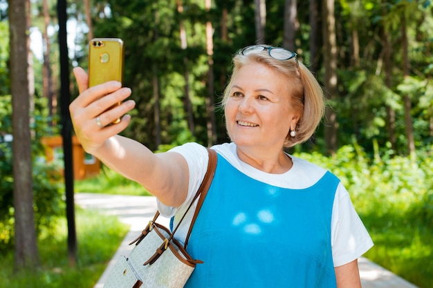 Portrait of a happy elderly woman taking selfies on a mobile phone in the park in summer