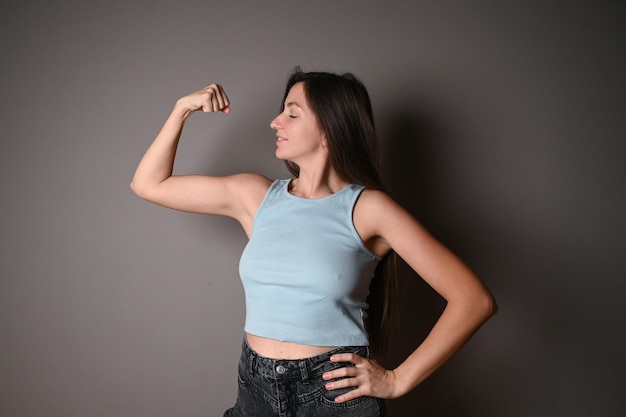 Portrait of a happy elegant woman showing her biceps on gray background Healthy lifestyle concept