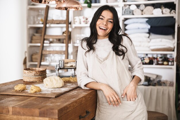 Portrait of happy european woman wearing apron cooking and making homemade pasta of dough in kitchen at home