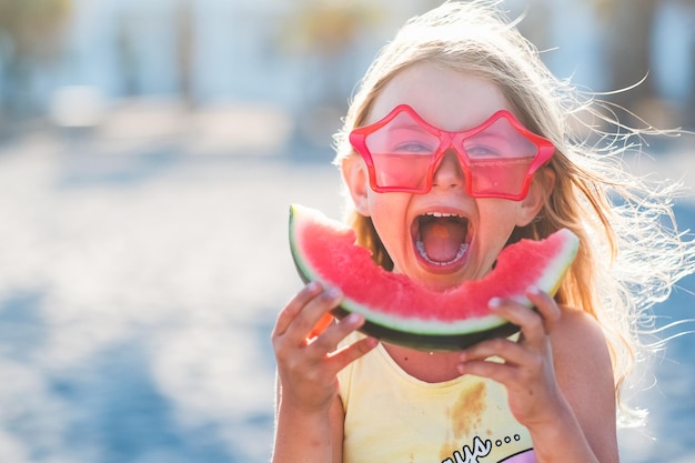 사진 세로 행복 흥분된 재미 있는 어린 소녀는 해변에서 주스 수박 조각을 먹고 여름과 야외 피크닉 개념 배너 복사 공간 장소 fot textisolated 자연 배경