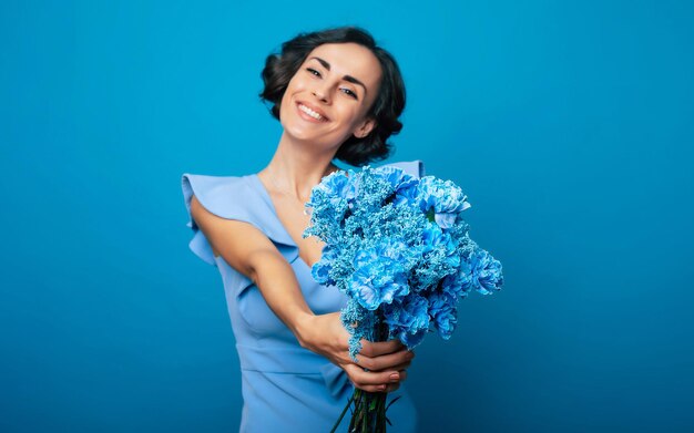 The portrait of a happy excited gorgeous young woman in an elegant blue dress is posing with a fresh bunch of blue flowers. Mothers day. Women's holidays. Springtime. Women rights