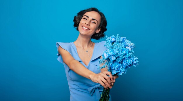 Il ritratto di una splendida giovane donna felice ed eccitata in un elegante vestito blu è in posa con un mazzo di fiori blu freschi festa della mamma vacanze delle donne primavera diritti delle donne