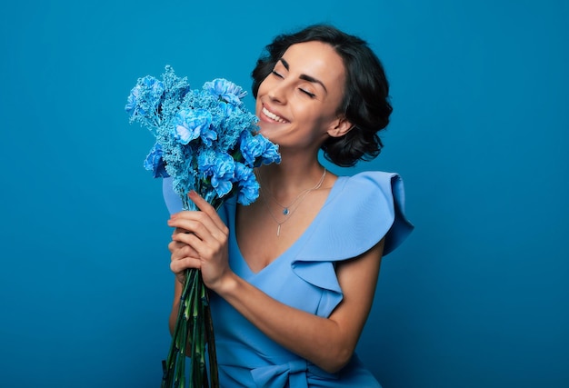 The portrait of a happy excited gorgeous young woman in an elegant blue dress is posing with a fresh bunch of blue flowers Mothers day Women's holidays Springtime Women rights