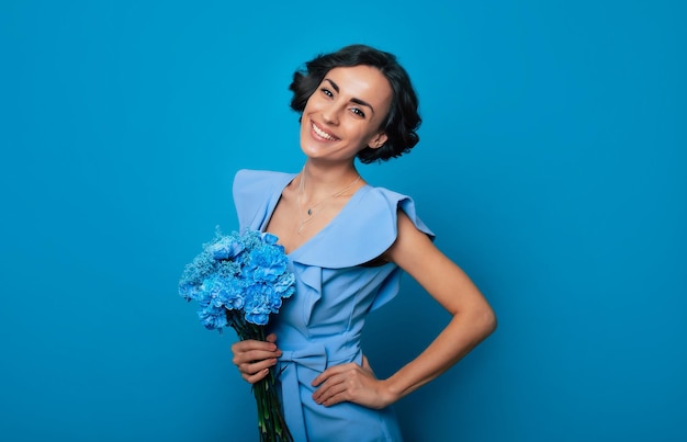 The portrait of a happy excited gorgeous young woman in an elegant blue dress is posing with a fresh bunch of blue flowers Mothers day Women's holidays Springtime Women rights