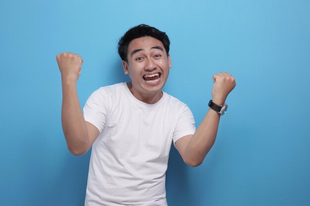 행복 한 흥분 된 젊은 아시아 남자 의 초상화 는 승리 한 몸짓 을 보여주고 미소 를 지으며 승리 를 축하 하고 있다