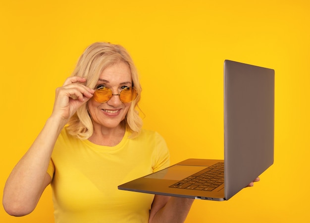 Photo portrait of happy exited abult lady with laptop isolated over the yellow studio.