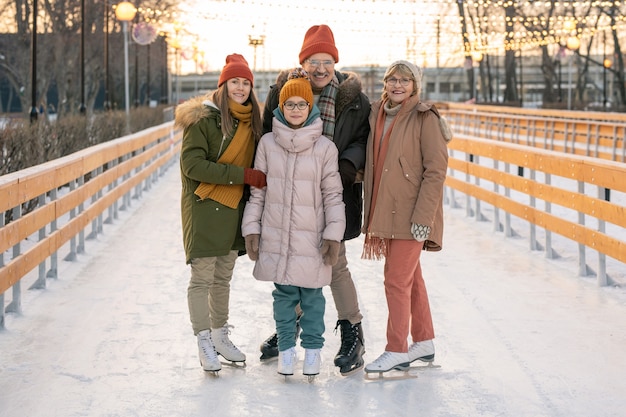 Портрет счастливой семьи, улыбаясь в камеру, стоя на катке и катаясь на коньках вместе
