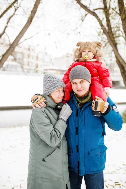 Portrait of happy family with one kid in winter casual outfit posing outdoors in snow public park