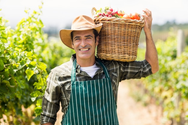 Portrait of happy farmer carrying a basket of vegetables