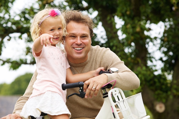 Portrait of happy father and daughter with bicycle in park