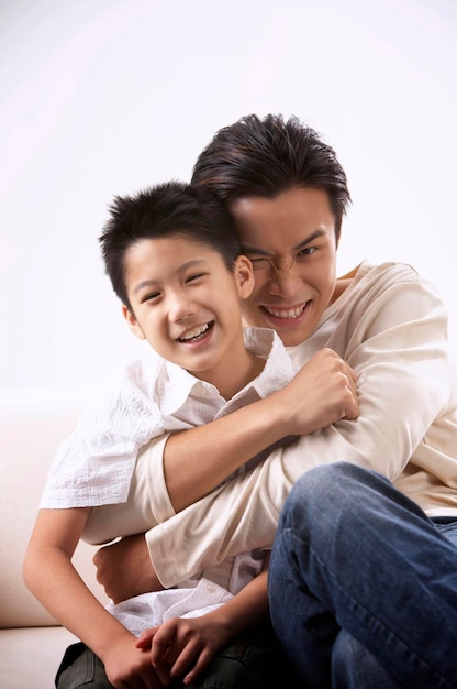 portrait of happy father and son sitting on sofa against white background