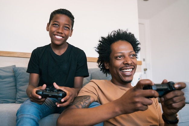 Portrait of happy father and son sitting in sofa couch and playing console video games together at home