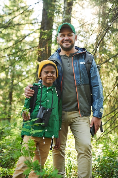 Portrait of happy father standing together with his son in the forest during their hiking