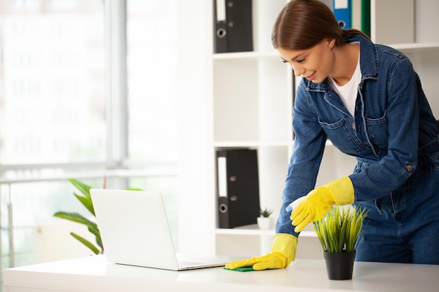 Portrait of happy female worker cleaning computer desk with spray and sponge at office