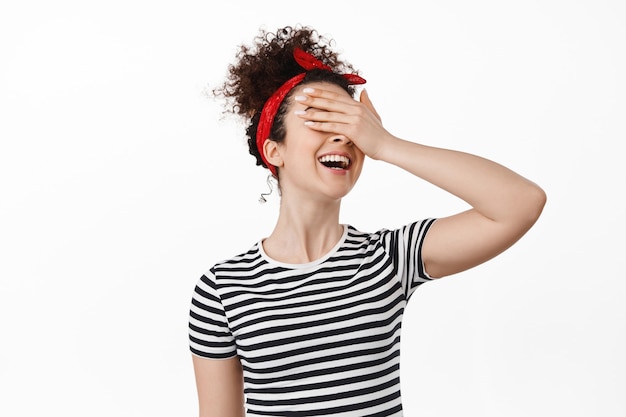 Portrait of happy feminst brunette curly woman with hand on eyes