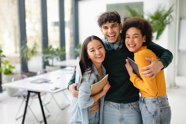 Portrait of happy friendly international college students embracing posing in coworking space free