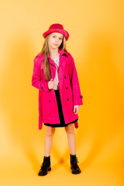 Photo portrait of happy girl in a raincoat and boots standing on yellow background