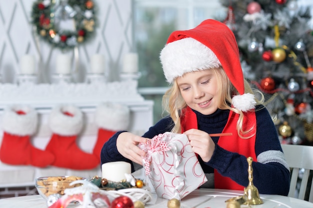 クリスマスプレゼントと一緒に座っているサンタ帽子の幸せな女の子の肖像画