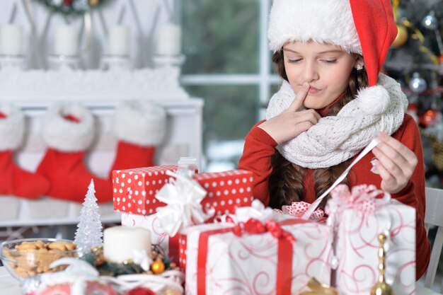 Portrait of happy girl in Santa hat sitting with Christmas presents