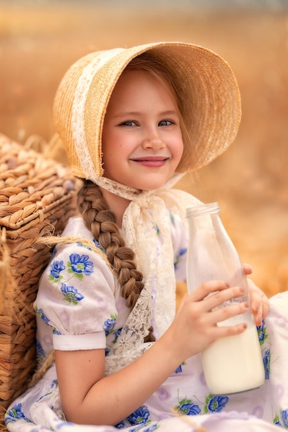 A portrait of a happy girl in a wheat field at sunset a child holds a glass jar with milk against