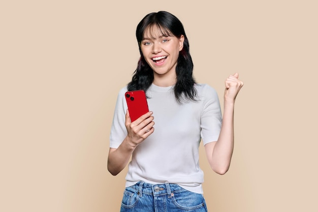 Portrait of happy girl with smartphone raising her fist up yes symbol