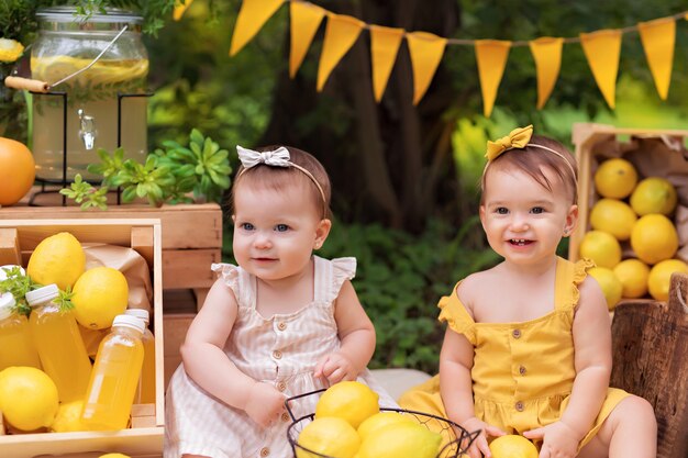 Portrait of happy girls sisters, baby eats lemons and drinks lemonade outdoors in summer