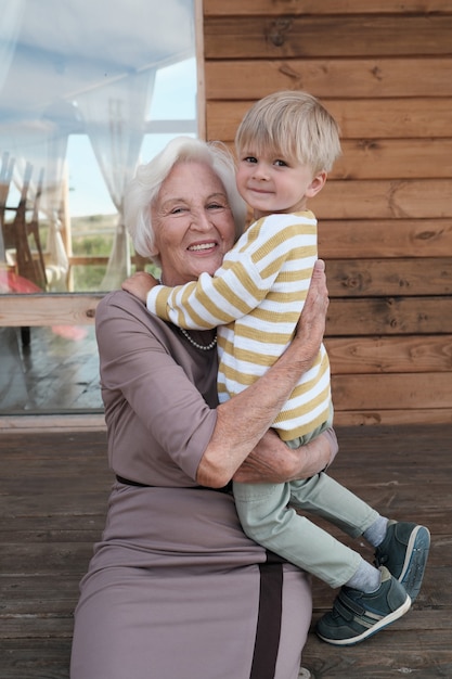 彼女の小さな孫を手に持って、屋外で笑っている幸せな祖母の肖像画