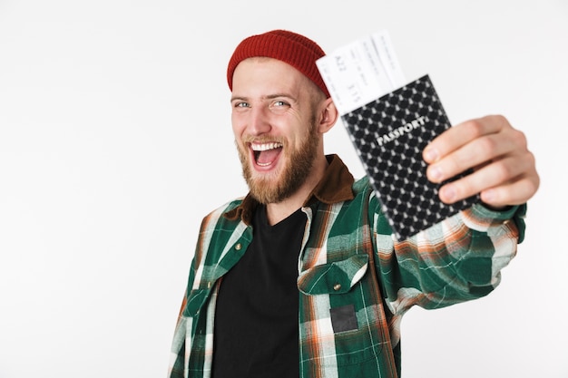 Photo portrait of happy guy wearing hat and plaid shirt holding passport and travel tickets, while standing isolated over white background