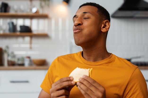 Photo portrait of happy handsome african american man holding tasty sandwich eating enjoying