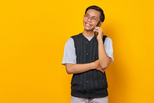 노란색 배경에서 휴대전화로 통화하는 행복한 잘생긴 아시아 남자의 초상화