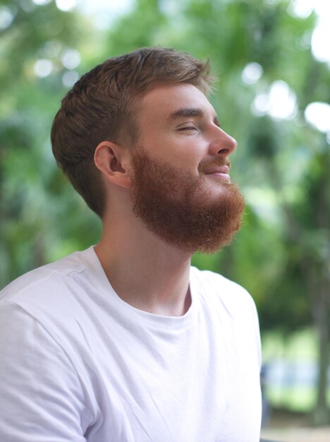 portrait happy handsome bearded young man in the park guy sit on a bench and enjoy warm fresh