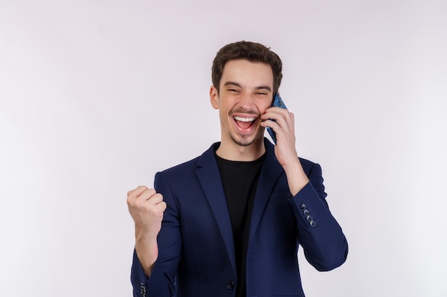 Photo portrait of happy handsome businessman talking by mobile phone and doing winner gesture clenching fist isolated over white background