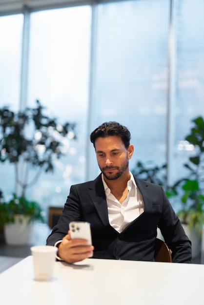 Portrait of happy handsome Hispanic businessman at coffee shop using phone