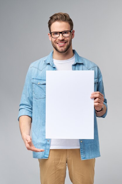 Portrait of a happy handsome young man holding blank white card or sign