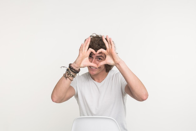 Portrait of happy handsome young man making heart with fingers on white background