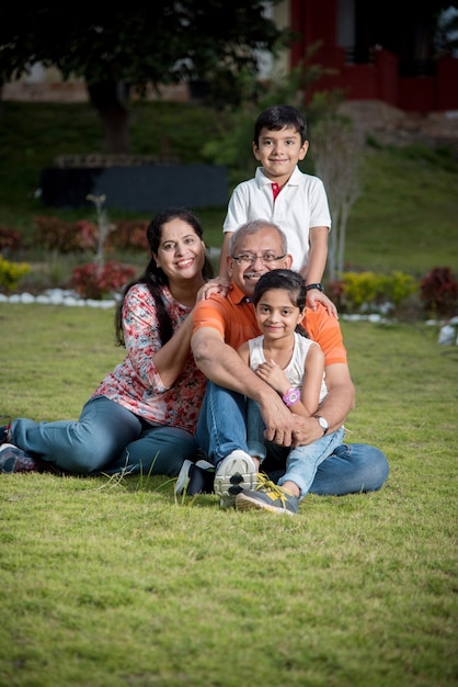 芝生に座って、屋外で幸せなインドのアジアの家族の肖像画
