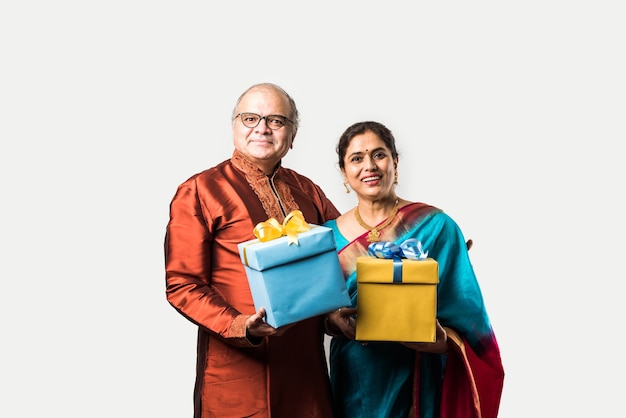 幸せなインドのアジアのシニアまたは白い背景で隔離のギフトボックスを保持している引退したカップルの肖像画